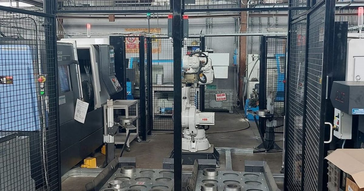 Machine tending cell: a fenced ABB robot between two lathes, with the parts pallet in the foreground
